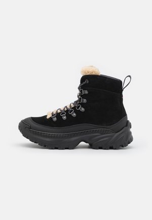 Botte de randonnée d’hiver noire avec semelle épaisse, devant lacée avec œillets métalliques et doublure en fourrure beige visible en haut.