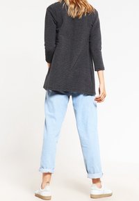 Mörkgrå, långärmad tunika med rundad nederkant bak, matchad med ljusblå jeans med upprullade ärmar och vita sneakers. Slät textur, avslappnad passform.