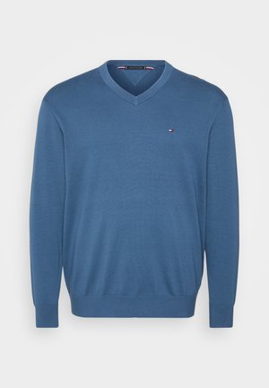 Pull bleu à col en V en tissu tricoté. Comprend des manches longues et des poignets côtelés. Petit logo accentué sur la poitrine gauche.