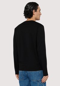 Czarna koszula z długim rękawem z bawełny, z klasycznym okrągłym dekoltem i gładką fakturą, w połączeniu z niebieskimi dżinsami.