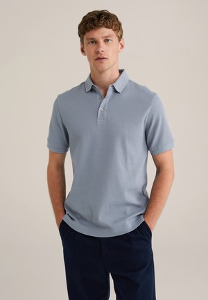 Lichtblauw geribbeld poloshirt met een kraag, drie knopen en korte mouwen, gedragen met donkerblauwe broek. Soepele textuur.