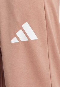 Lyserøde bomuldsbukser med en struktureret stof og et fremtrædende hvidt tre-stribes logo designet på låret.