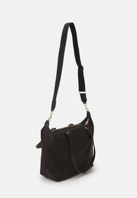 Black fabric handbag with dual handles, adjustable shoulder strap, gold hardware, zip closure, and streamlined design.