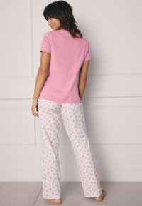 Roze top met korte mouwen gecombineerd met witte broek met een verspreid hartpatroon. De stof lijkt zacht en comfortabel te zijn.