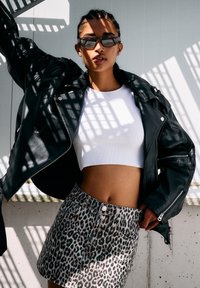 Zwarte leren motorjack over een witte cropped top, gecombineerd met een beige denim rok met luipaardprint. Zonnebrillen en schaduwen zorgen voor contrast.