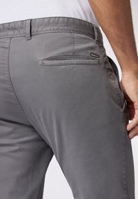 Pantaloni grigi realizzati in tessuto liscio, dotati di una tasca posteriore, passanti per cintura e una vestibilità slim. Minima presenza di cuciture e dettagli in metallo.