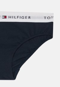 Marineblauwe katoenen slip met een witte elastische tailleband waarop de zwarte opdruk "TOMMY HILFIGER" staat, en een gladde, zachte textuur.