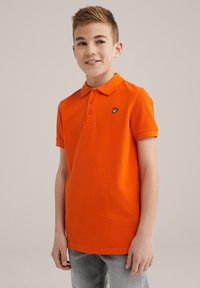 Pomarańczowa koszulka polo z kołnierzykiem, krótkimi rękawami, trzema guzikami oraz małym czarnym haftowanym logo na lewej piersi.