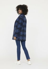 Blauwe geblokte oversized jas van textiel, met een kraag en knopen aan de voorkant, gecombineerd met aansluitende spijkerbroek en sneakers.