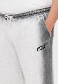 Grå og off-white gradient joggebukser med elastisk liv, snøring, sidelommer og en svart logo på venstre lår.
