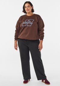 Ruda džemperis su šviesiai mėlynu užrašu „playful“, derinamas su juodomis kelnėmis ir bordo sportbačiais. Laisvo silueto, minkštos medžiagos ir kasdienio stiliaus.