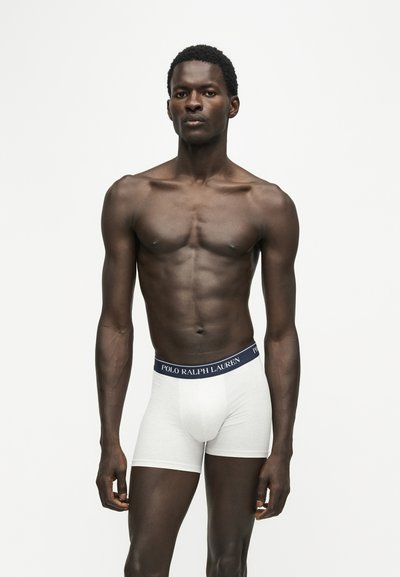 Αθλητικός άνδρας που φορά λευκά boxer briefs Polo Ralph Lauren στέκεται μπροστά σε λευκό φόντο, κοιτάζοντας μπροστά με ουδέτερη έκφραση.