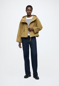 Sárga vízálló kapucnis dzseki cipzárral, első zsebekkel és húzózsinórral. Fehér és tengerészkék csíkos inggel és sötét farmernadrággal párosítva.