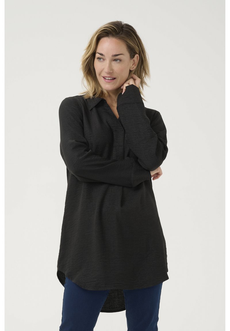 Schwarzes Langarmshirt mit Kragen, strukturiertem Stoff und abgerundetem Saum, kombiniert mit blauen Hosen.