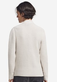 Biały sweter z dzianiny o teksturowanym wzorze, w luźnym kroju, z długimi rękawami i kołnierzykiem, widoczny z tyłu.