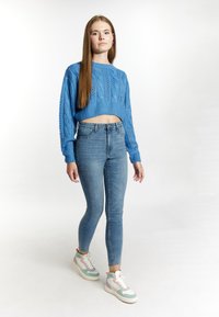 Pulover scurt din tricot cu model cable, asociat cu blugi skinny de culoare albastru deschis și adidași multicolori. Design simplu, croială lejeră, material texturat.