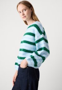 Blauwe en groene gestreepte trui met een fuzzy textuur, voorzien van losse mouwen en een ontspannen pasvorm. Gecombineerd met donkere spijkerbroeken.