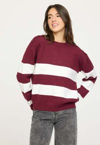 Pull bordeaux et blanc à rayures avec un col rond, des épaules tombantes et des boutons sur l'épaule. Texture en tricot douce.