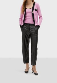 Růžový žebrovaný cardigan s černými akcenty, doplněný o sladěný top bez rukávů a volné černé kožené kalhoty. Celkový vzhled doplňují černé lodičky na podpatku.