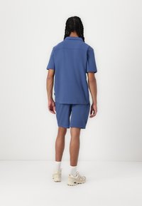 Polo à manches courtes et shorts assortis en tissu bleu clair uni. La tenue présente une coupe décontractée, des coutures plates et un design minimaliste.