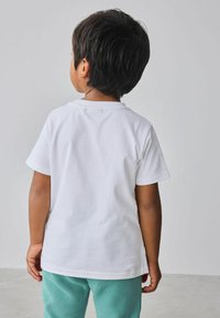 Biele bavlnené tričko s krátkymi rukávmi, okrúhlym výstrihom a voľným strihom, doplnené tyrkysovými teplákmi. Jednoduchá a hladká textúra.