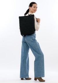 Juodas kuprinės iš geometrinių raštų su petnešėlėmis, stačiakampio formos, su tekstūruota paviršiaus ir subtiliu prekės ženklo akcentu apačioje.