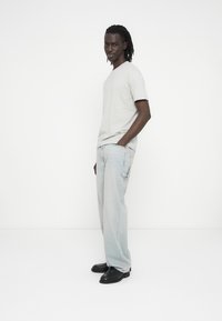 Light gray short-sleeve T-shirt, relaxed fit; paired with light blue loose-fit jeans featuring distressed accents; black leather shoes.