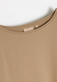 Brązowy top z krótkim rękawem i okrągłym dekoltem, wykonany z miękkiej, gładkiej tkaniny; metka widoczna z tyłu z oznaczeniem rozmiaru.