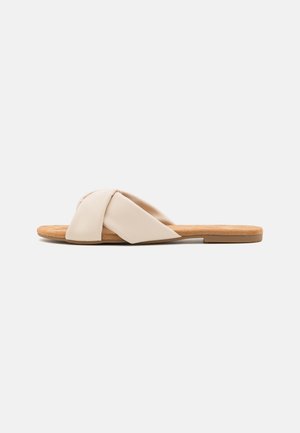 Beige flade slip-on sandal med en knyttet syntetisk overdel, læderindersål og struktureret brun ydersål. Enkel design, åben tå stil.