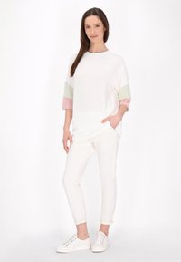 Tunică albă supradimensionată cu mâneci scurte, în dungi roz pal și verde deschis, asociată cu pantaloni albi evazați și teniși albi.
