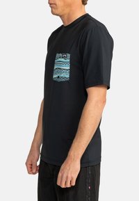 Svart kortärmad t-shirt i bomull med en mönstrad ficka med blå och gröna geometriska mönster.