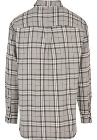 Grijs geruite blouse met lange mouwen, voorzien van een achterste schouderpas, contrasterende witte en donkergrijze lijnen, knoopdetails op de manchetten en een zachte stoftextuur.