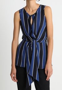 Mörkblå ärmlös blus med vita vertikala ränder, featuring en nyckelhålsöppning fram och en knutig nederkant. Slät tygkvalitet med en avslappnad passform.