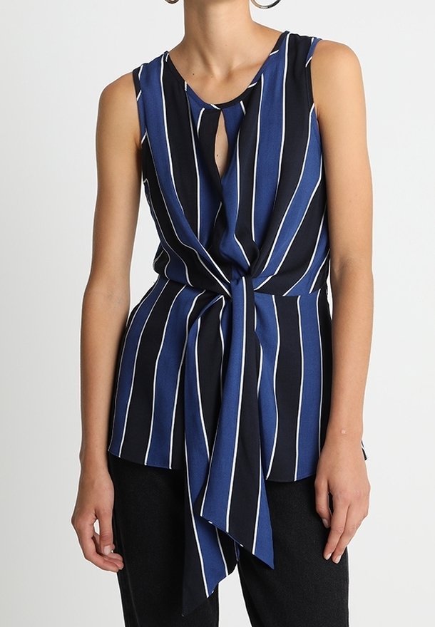 Mörkblå ärmlös blus med vita vertikala ränder, featuring en nyckelhålsöppning fram och en knutig nederkant. Slät tygkvalitet med en avslappnad passform.