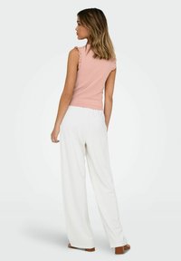 Ljusrosa ärmlös topp med ruffle-detaljer, i kombination med vita vida byxor, som visar en slät textur och en figurnära design.