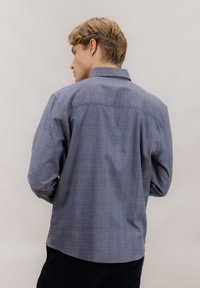 Blå rutete skjorte med knapper, langermet og med krage, laget av et teksturert stoff og med rett kant bak.