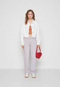 Chaqueta corta blanca con perforaciones, top naranja con patrón ondulado, pantalones lavanda, bolso rojo en forma de corazón y zapatillas blancas con detalles rojos.