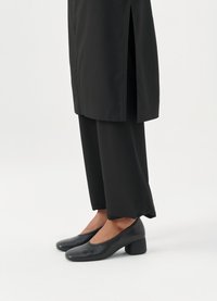 Pantofi cu toc negru, cu o textură lucioasă embosată în croc, având vârful rotunjit și un toc solid de tip block. Asociați cu pantaloni negri cu picior larg.