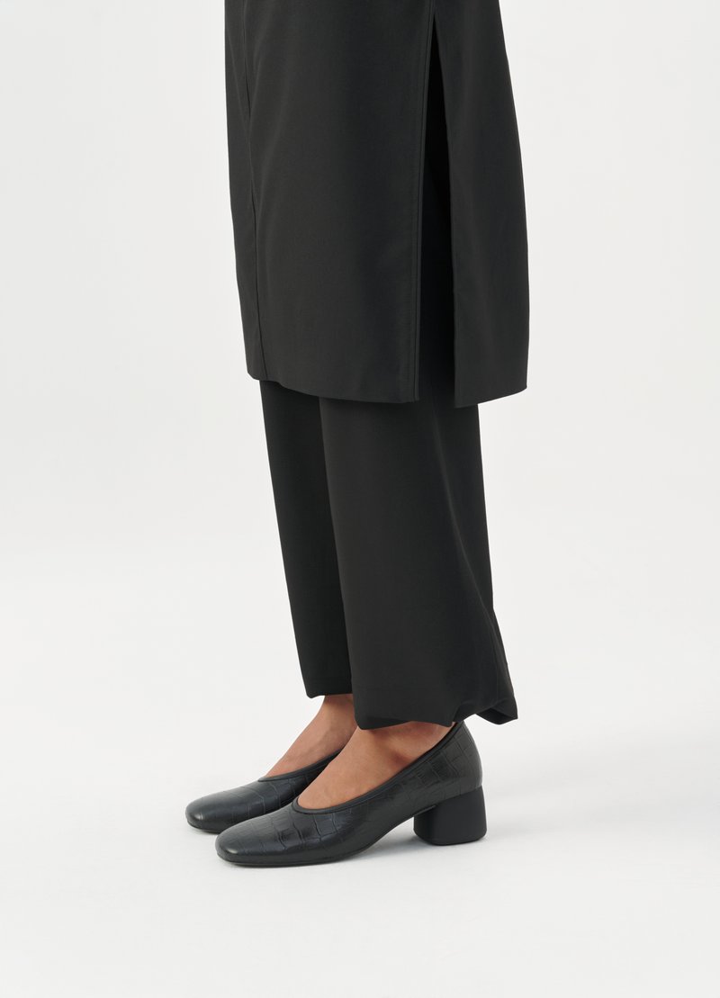 Schwarze High Heels mit glänzender Krokodilprägung, runder Zehenpartie und stabilen Blockabsätzen. Kombiniert mit schwarzen, weit geschnittenen Hosen.