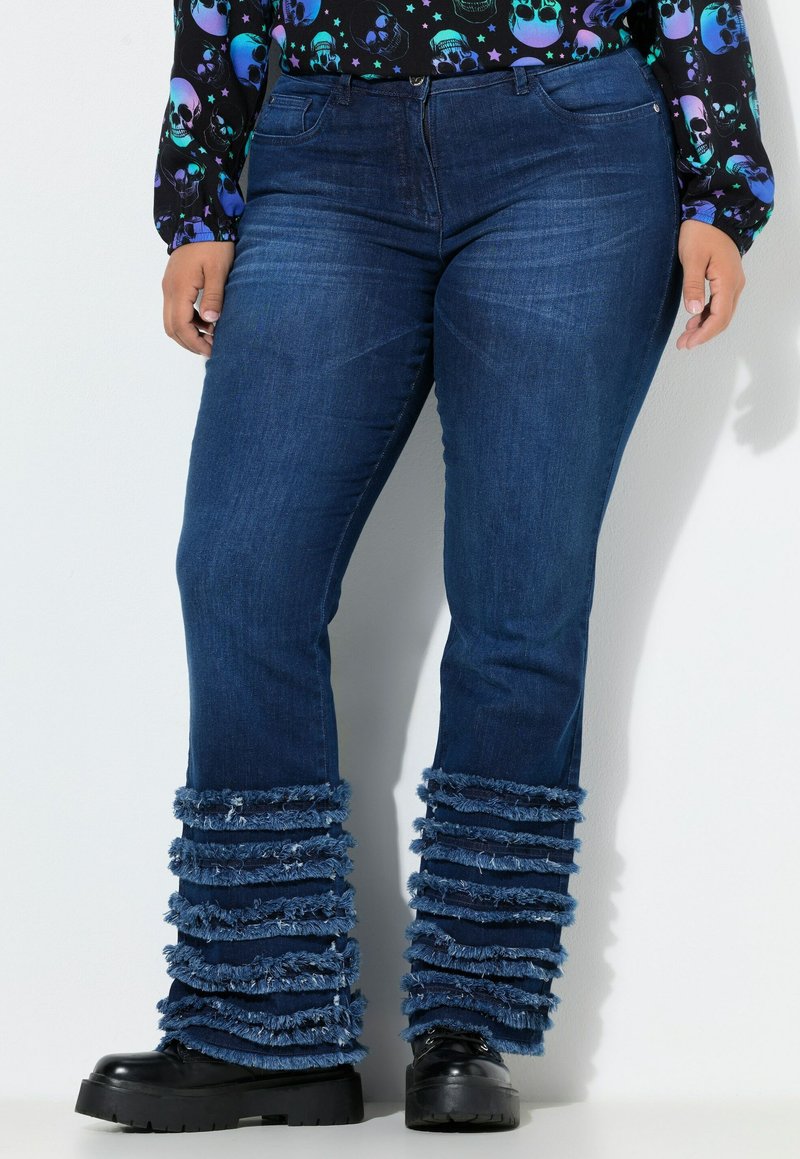 Jeans in denim con un lavaggio blu scuro, con accenti frangiati all'orlo in blu chiaro. Abbinati a stivali platform neri.