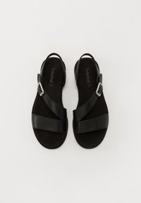 Sandalias pretas com sola plana, apresentando duas tiras em couro cruzadas e um detalhe com fivela prateada. Palmilha macia e texturizada para conforto.