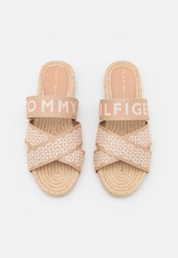 Sandales espadrilles rose pâle avec des brides en tissu croisées, arborant un logo blanc et des motifs géométriques sur la semelle.