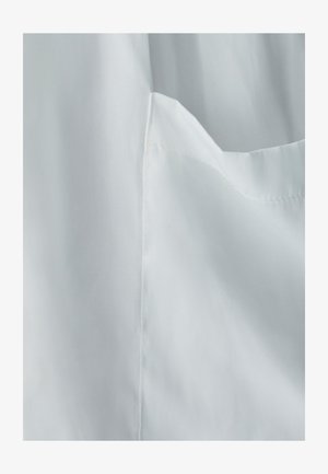 Hvidt stof med en glat tekstur. En lomme er synlig på venstre side, med pæne sømme og en let glans.