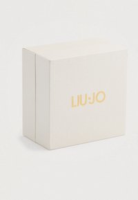 Kreemikollane tekstuuriga karp, mille esifaas on tsentreeritud kuldne "LIU·JO" logo, asetatud valgele taustale.