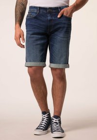 Tummansiniset farkkushortsit, joissa on käännetyt lahkeet, viisi taskua ja napitus. Yhdistetty tummansinihin korkeisiin tennareihin.