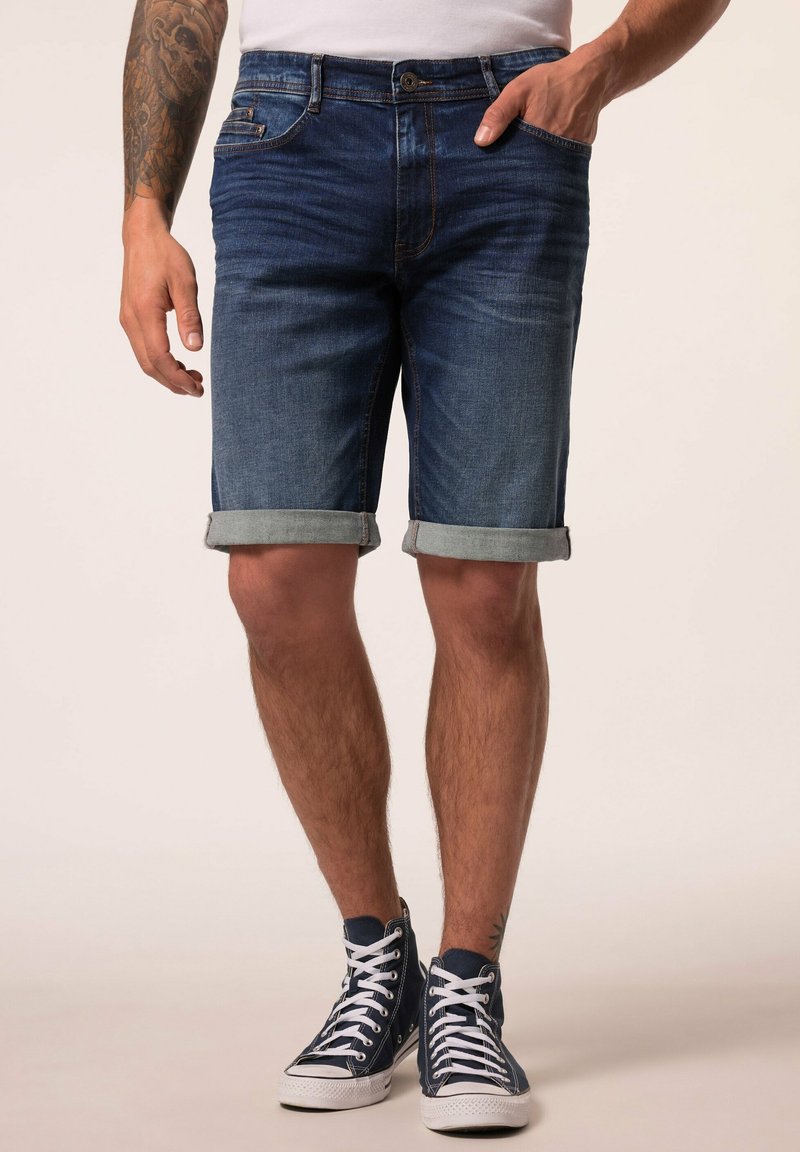 Tummansiniset farkkushortsit, joissa on käännetyt lahkeet, viisi taskua ja napitus. Yhdistetty tummansinihin korkeisiin tennareihin.