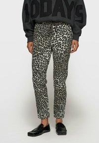 Pantalons à imprimé léopard dans des nuances de gris et de noir, présentant une coupe slim avec une taille élastique et un cordon de serrage, associés à des chaussures noires.