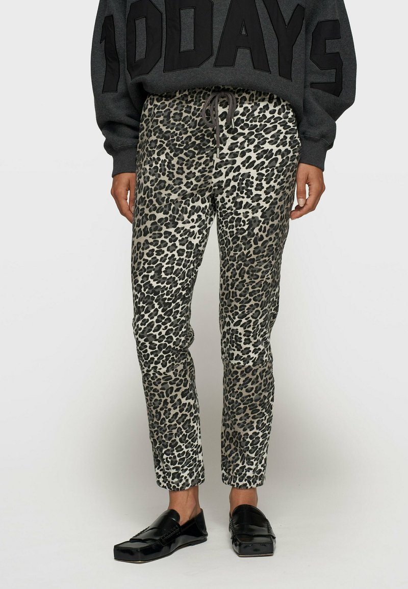 Pantalons à imprimé léopard dans des nuances de gris et de noir, présentant une coupe slim avec une taille élastique et un cordon de serrage, associés à des chaussures noires.