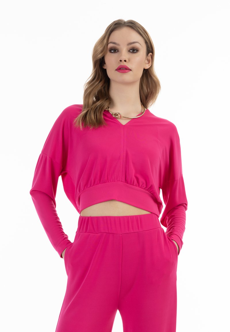 Top lungo corto rosa con maniche lunghe, scollatura a V e orlo arricciato, abbinato a pantaloni a vita alta coordinati. Tessuto morbido e elasticizzato.