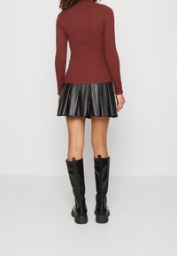 Czerwony prążkowany golf, czarna plisowana mini spódnica z sztucznej skóry i czarne kozaki sięgające kolan. Charakteryzuje się teksturowanym materiałem i warstwowym designem.